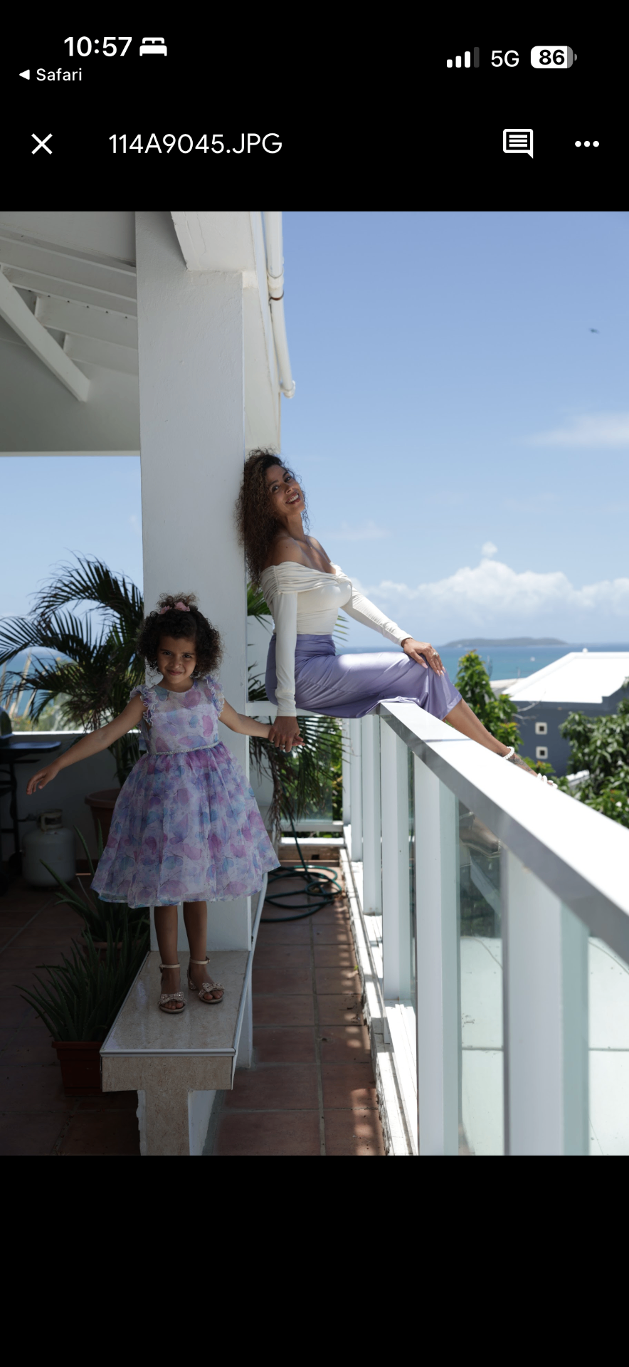 Jennifer Rivera and her daughter standing close together on a bright coastal balcony, looking out toward the ocean.